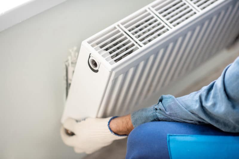 A picture of a worker installing a radiator inside a residential home
