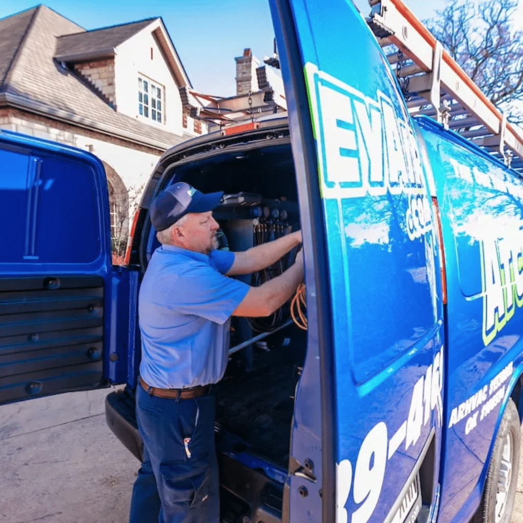 An Atchley Air employee at the rear side of a Atchley Air service van with the door open retrieving tools from the inside of the van