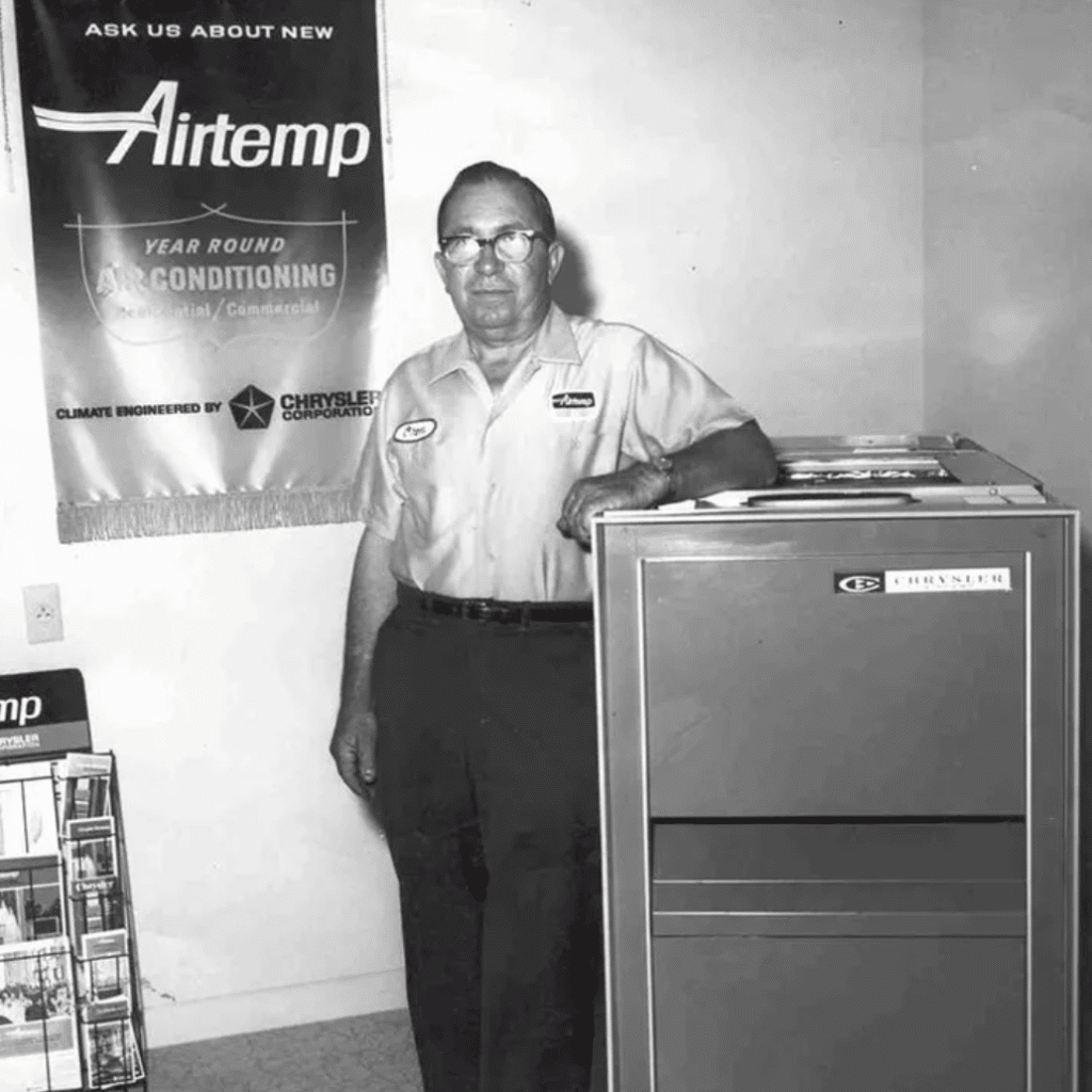 A greyscale picture of Oren Atchley standing next to a Chrysler Air Conditioning unit