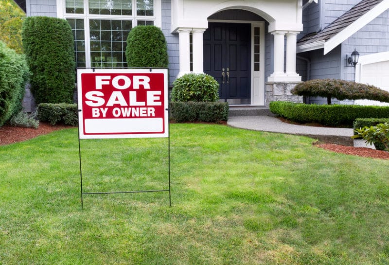 Front view of a house with a sign in the front yard that reads For Sale By Owner