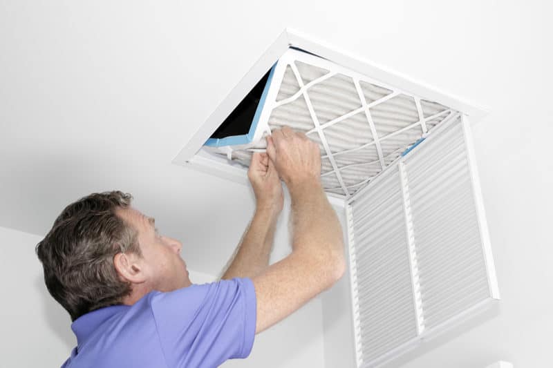 Male removing an air filter from a ceiling air vent
