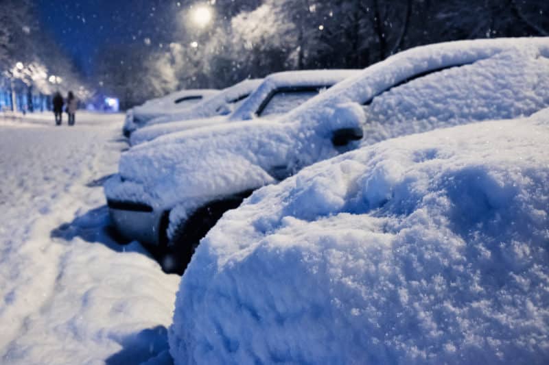 A row of cars in a parking lot under a thick blanket of snow